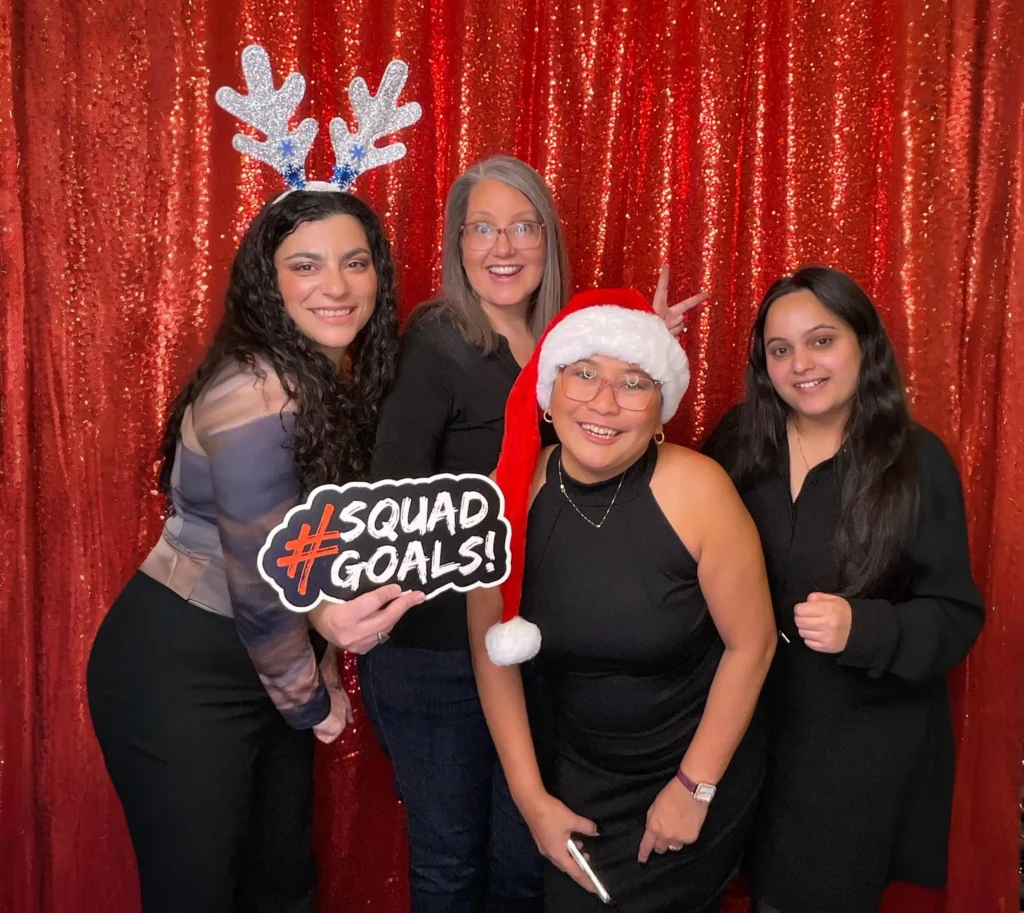 Group of coworkers posing with festive props in front of a red sequin photo booth backdrop